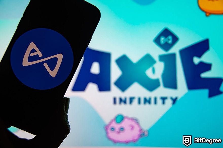 Game NFT terbaik: Logo Axie Infinity dan seseorang memegang ponsel.