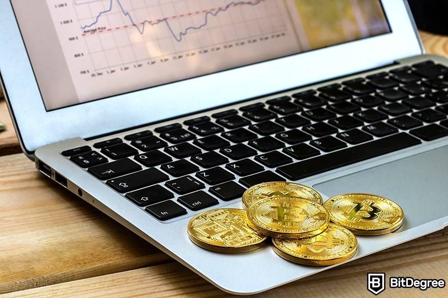 Apa itu uang fiat dalam crypto: Bitcoin berbentuk fisik diatas laptop yang memperlihatkan data pasar.