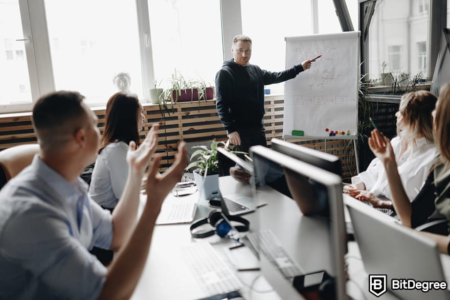 Web3 işleri: bir kişinin ofis ortamında bir grup insanın önünde bir grafiği sunduğu bir toplantı.