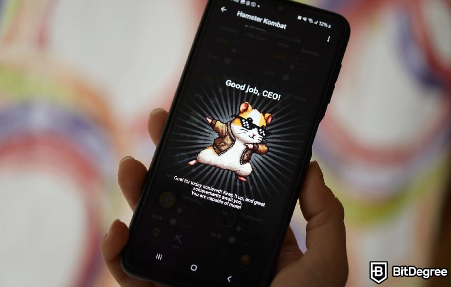 什么是 Hamster Kombat：一个人拿着手机，屏幕上显示 Hamster Kombat CEO 页面。